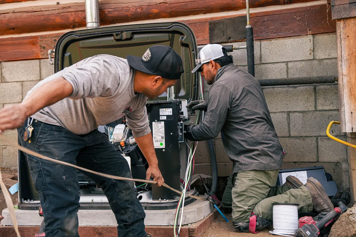 Two Apex technicians working inside the open enclosure of a standby generator