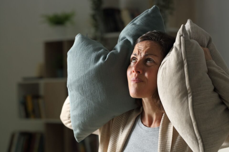 woman covering her ears with throw pillows as she looks up in the direction of a loud air vent