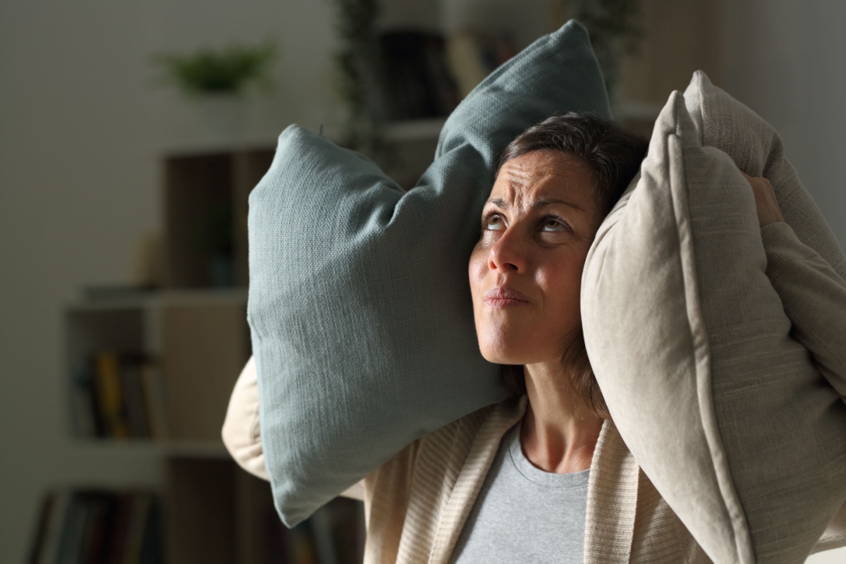 woman covering her ears with throw pillows as she looks up in the direction of a loud air vent