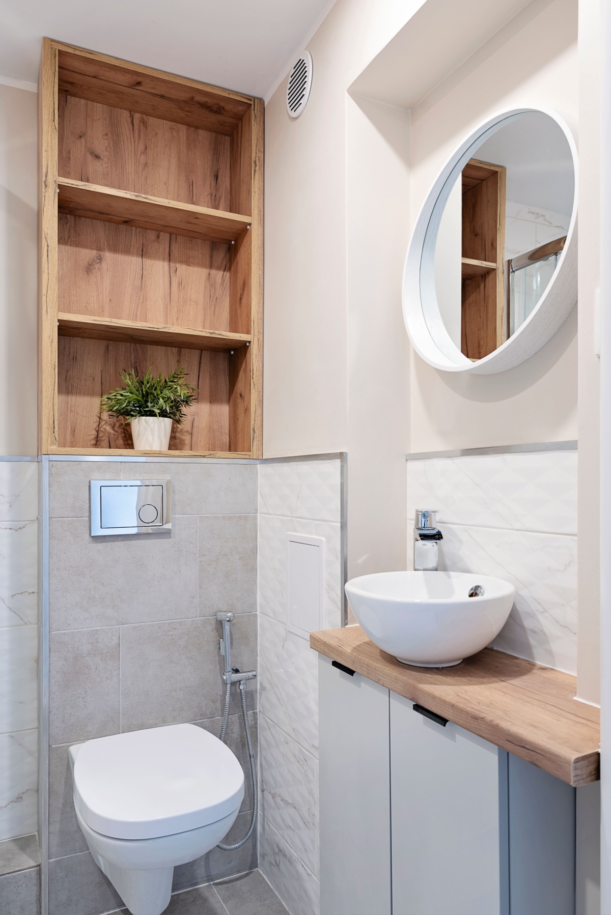 A small, compact bathroom remodeled to maximize space with a stone accent wall, vertical shelving unit, floating sink, and round mirror.