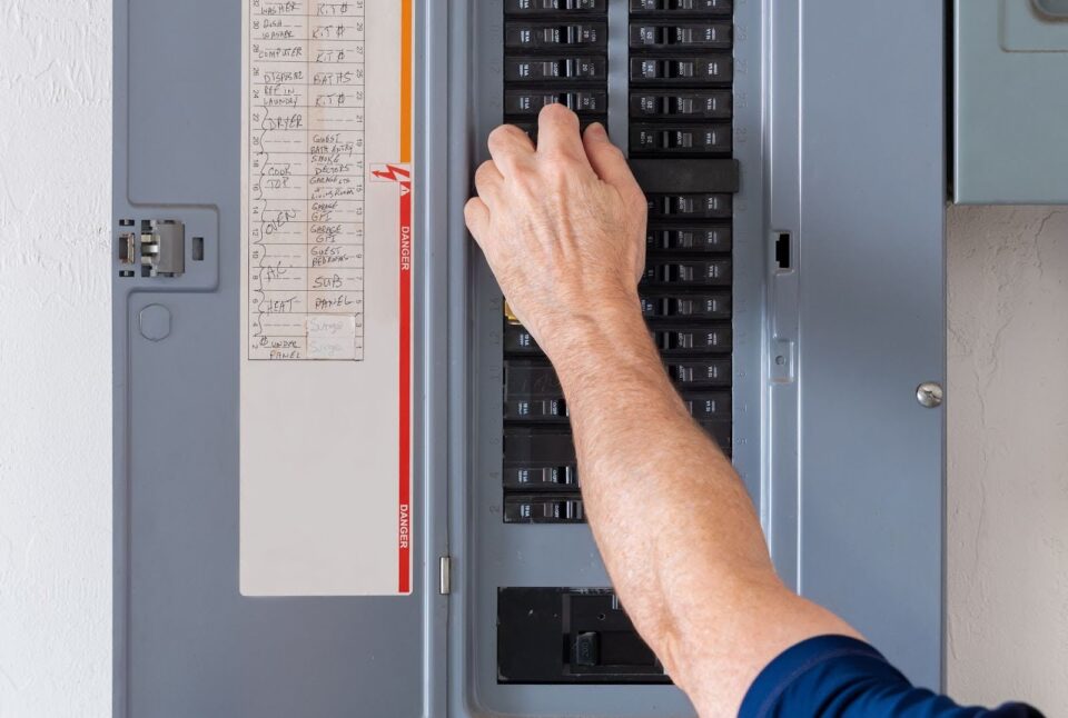 An electrician's hand checking the circuit on an electrical panel