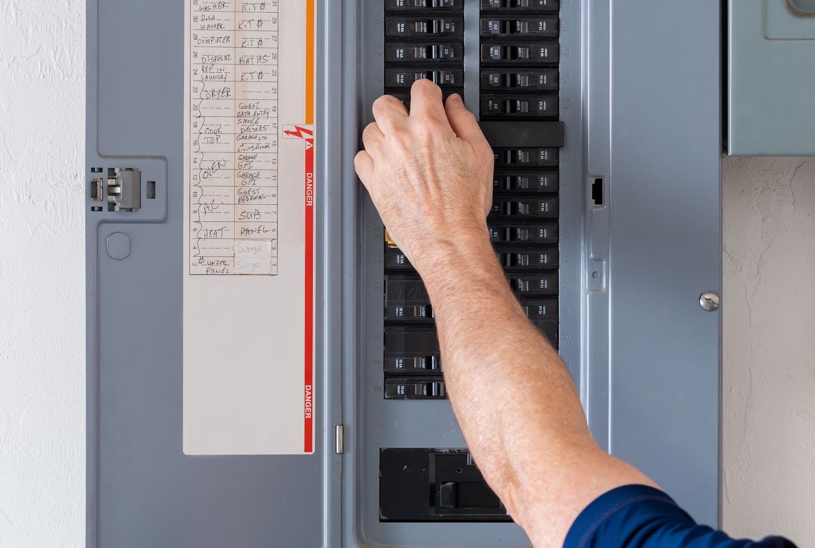 An electrician's hand checking the circuit on an electrical panel